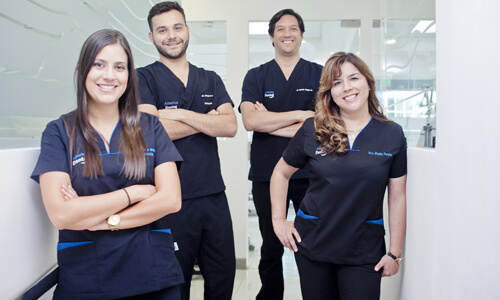 Picture of a dental team representing the dental services of the Costa Rica Dental Center in San Jose, Costa Rica.  The team consists of 2 male dentists and 2 female dentists, who are wearing dark blue work uniforms.