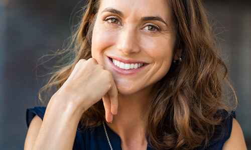Picture of a smiling woman, happy with the cosmetic dental treatments she had at the Costa Rica Dental Center in San Jose, Costa Rica.  The woman has long brown hair and is wearing a black blouse.  She has perfect teeth and is smiling directly at the camera.